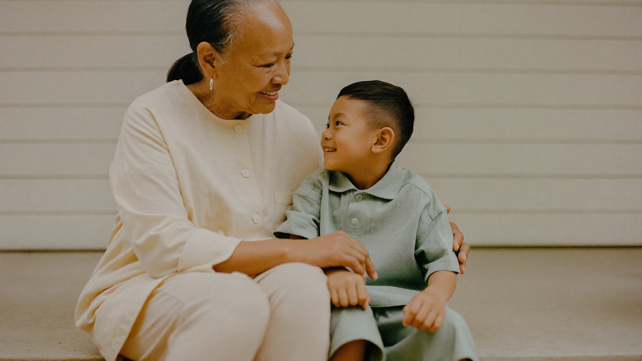 A grandmother and her young grandson sitting together on a porch step, sharing a smile